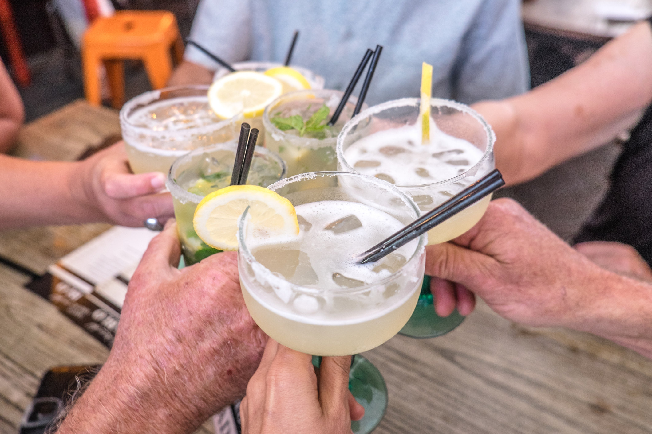 Hands young and old celebrating making a toast and clinking cocktail glasses with margaritas and mojito drinks at celebration