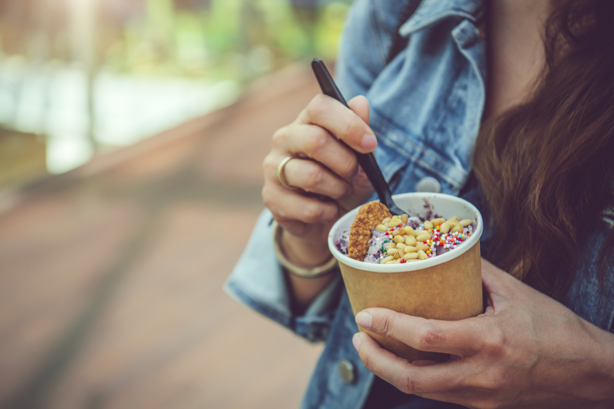 Young woman eating healthy rolled ice-cream or yogurt with fruits or berries, cookies, candy and mint